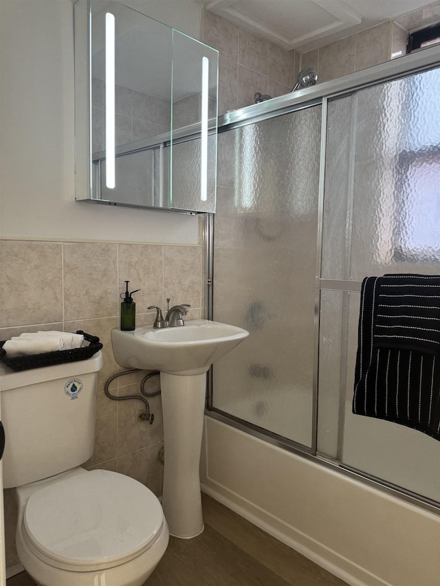 bathroom with tile walls, shower / bath combination with glass door, toilet, and wood finished floors