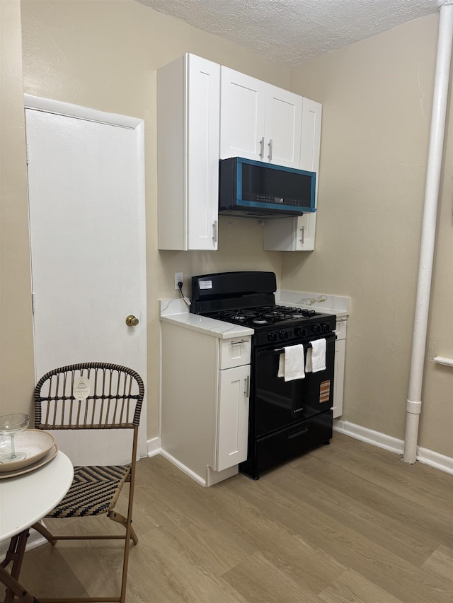 kitchen with black appliances, light wood-type flooring, white cabinets, light countertops, and baseboards