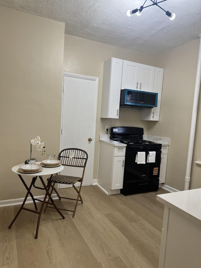 kitchen with black range with gas stovetop, light wood finished floors, a textured ceiling, light countertops, and white cabinetry