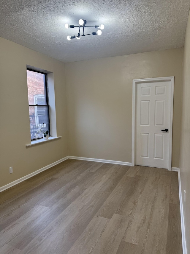 empty room featuring wood finished floors, a textured ceiling, and baseboards