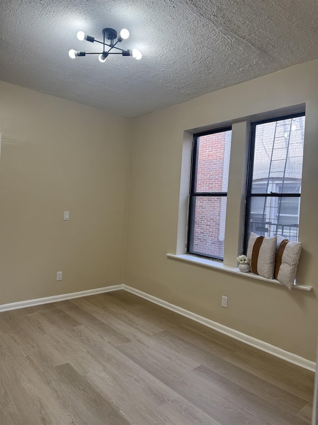 spare room with wood finished floors, a textured ceiling, baseboards, and a chandelier