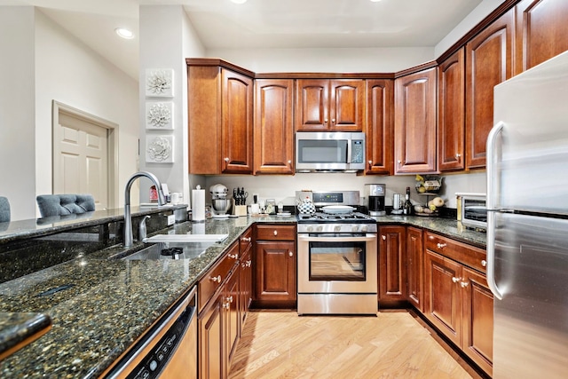 kitchen featuring sink, stainless steel appliances, light hardwood / wood-style floors, and dark stone counters