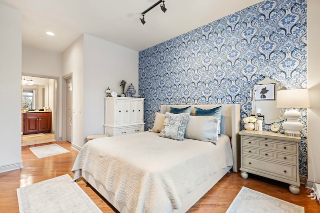 bedroom featuring track lighting, connected bathroom, and hardwood / wood-style flooring