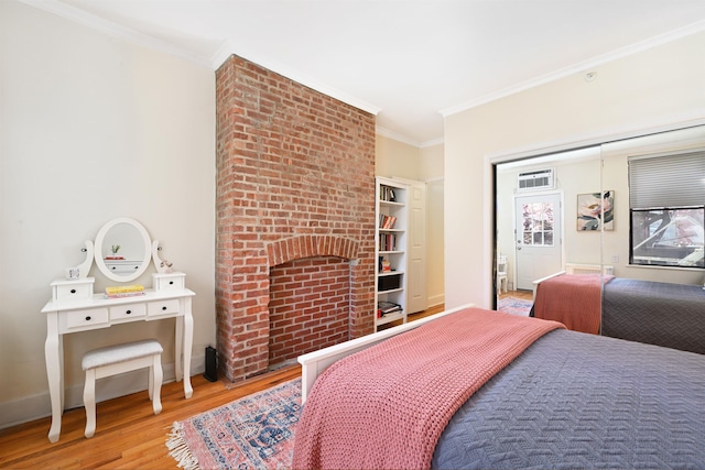 bedroom featuring ornamental molding, wood finished floors, baseboards, and a brick fireplace
