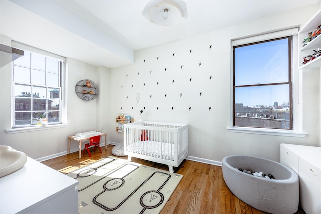 bedroom featuring a nursery area, wood finished floors, and baseboards