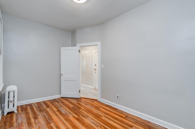 unfurnished room featuring light wood-style floors, baseboards, and radiator heating unit