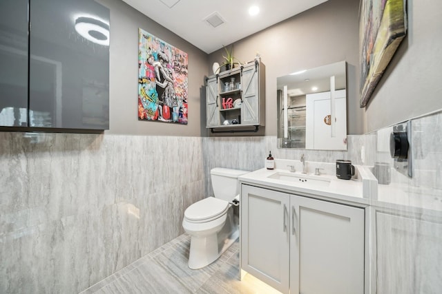 bathroom featuring tile patterned flooring, vanity, toilet, and tile walls