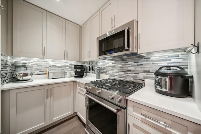 kitchen with tasteful backsplash, dark hardwood / wood-style flooring, white cabinets, and appliances with stainless steel finishes