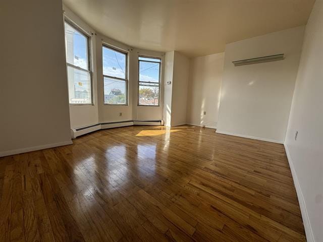 spare room featuring wood-type flooring, a baseboard radiator, and basketball hoop