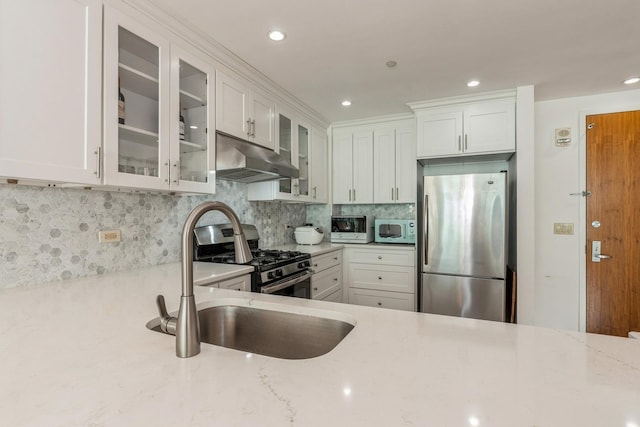 kitchen featuring appliances with stainless steel finishes, white cabinetry, sink, backsplash, and light stone countertops