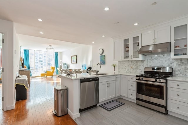 kitchen with appliances with stainless steel finishes, kitchen peninsula, sink, and white cabinets