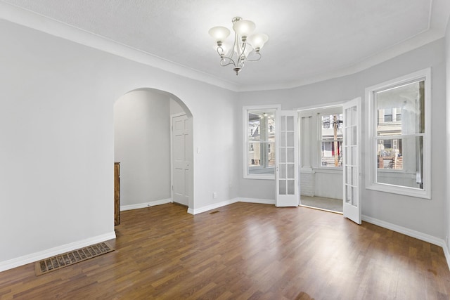 spare room with baseboards, visible vents, arched walkways, wood finished floors, and a notable chandelier