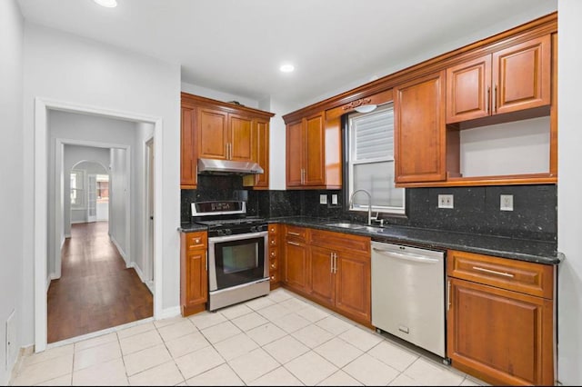 kitchen featuring arched walkways, stainless steel appliances, decorative backsplash, a sink, and under cabinet range hood