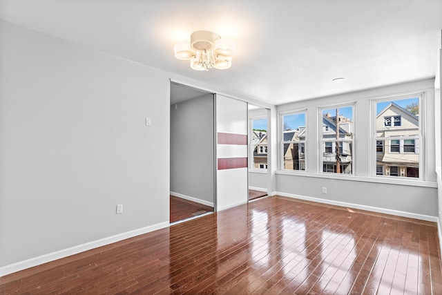 empty room featuring an inviting chandelier, baseboards, and hardwood / wood-style flooring