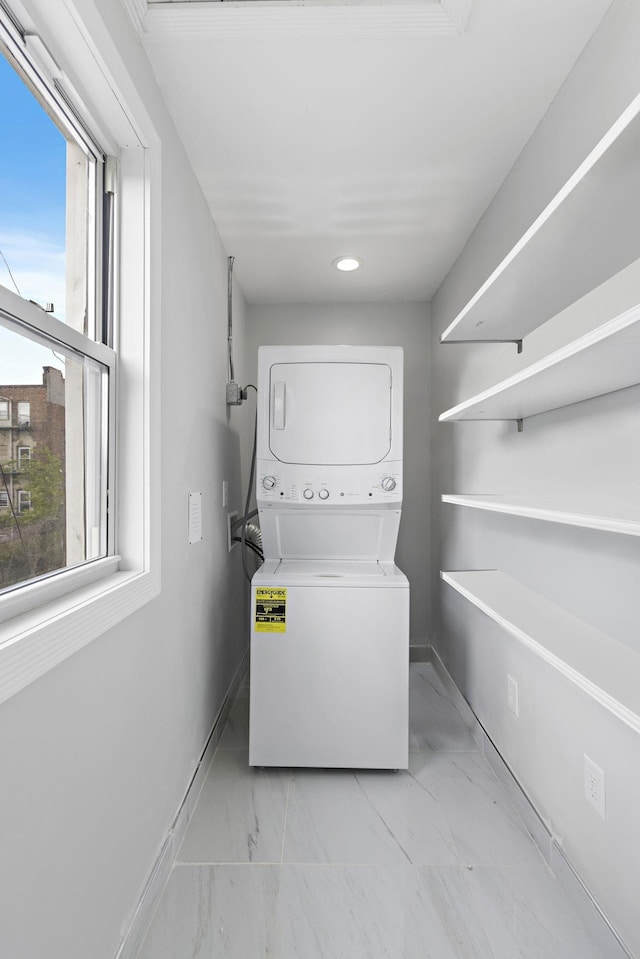 laundry room featuring baseboards, laundry area, plenty of natural light, and stacked washer / drying machine