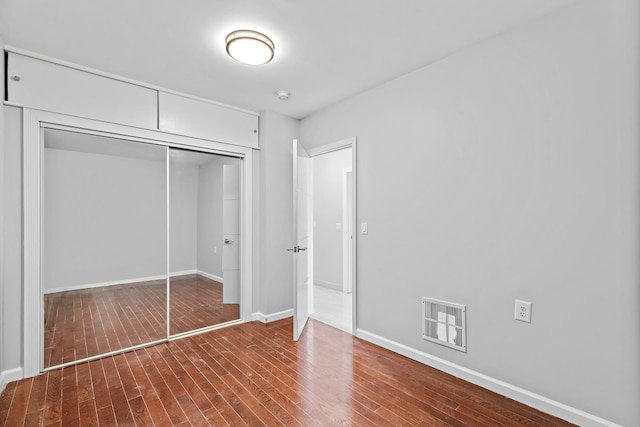 unfurnished bedroom with hardwood / wood-style floors, baseboards, visible vents, and a closet