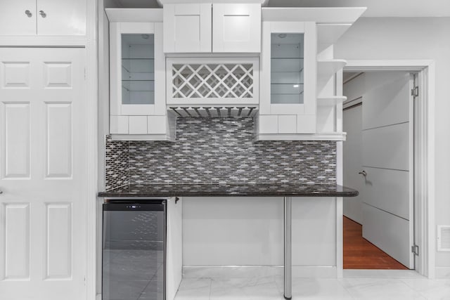 kitchen featuring beverage cooler, white cabinets, backsplash, and dark stone countertops