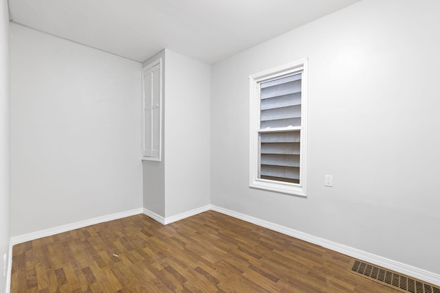 empty room with dark wood-style flooring, visible vents, and baseboards