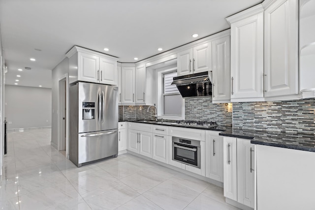 kitchen with dark countertops, range hood, stainless steel appliances, white cabinetry, and a sink