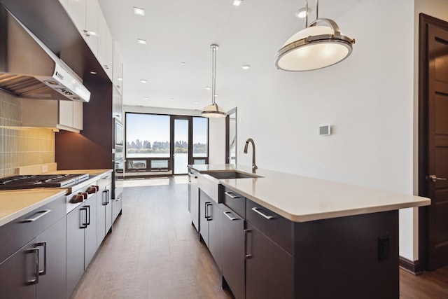 kitchen featuring extractor fan, decorative light fixtures, white cabinets, and a large island with sink