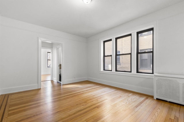 empty room with a wealth of natural light, light wood-type flooring, radiator, and baseboards