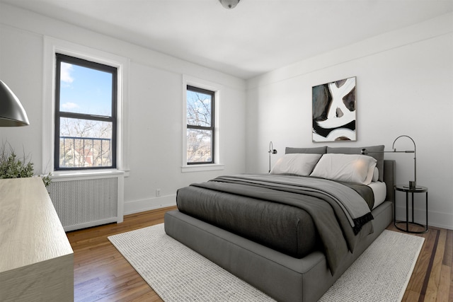 bedroom featuring radiator, multiple windows, baseboards, and wood finished floors