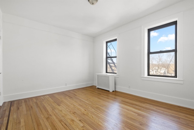 unfurnished room featuring radiator, light wood-style floors, and baseboards