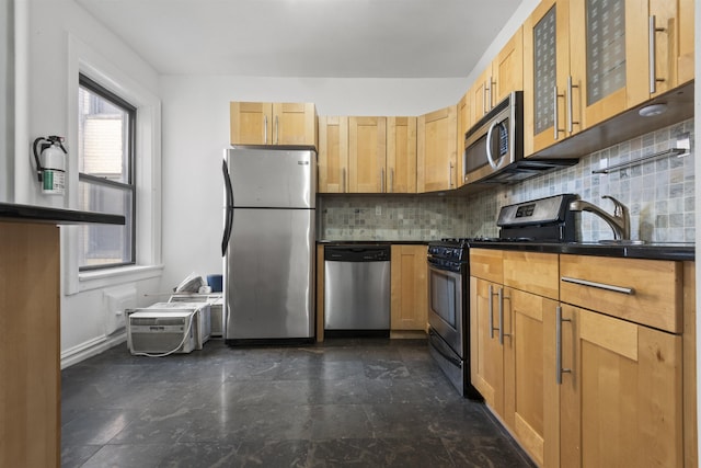 kitchen featuring stainless steel appliances, a sink, backsplash, dark countertops, and glass insert cabinets