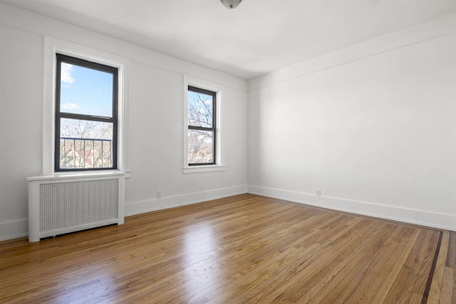 empty room featuring radiator, light wood finished floors, and baseboards