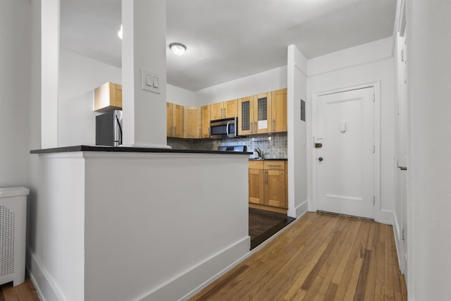 kitchen featuring dark countertops, wood-type flooring, backsplash, appliances with stainless steel finishes, and glass insert cabinets