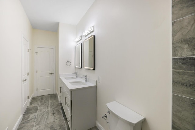 bathroom with double vanity, baseboards, toilet, marble finish floor, and a sink