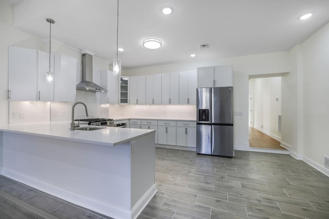 kitchen featuring wall chimney exhaust hood, tasteful backsplash, a peninsula, and stainless steel fridge