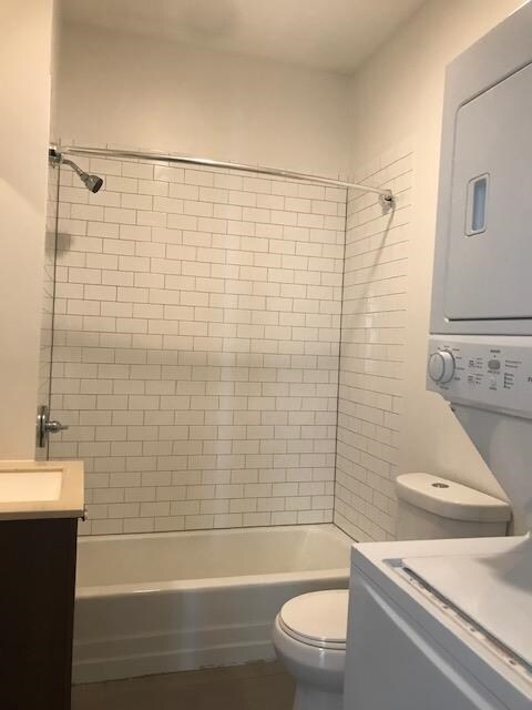 full bathroom with toilet, tiled shower / bath combo, stacked washer and clothes dryer, and vanity