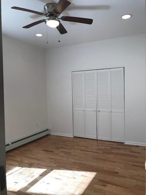 unfurnished bedroom featuring ceiling fan, a baseboard radiator, a closet, and wood-type flooring