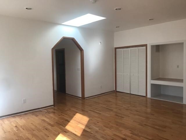 unfurnished bedroom featuring hardwood / wood-style floors, built in desk, and a skylight