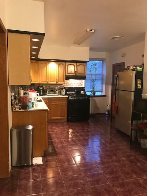 kitchen featuring dark tile patterned flooring, kitchen peninsula, black range with gas cooktop, backsplash, and stainless steel refrigerator