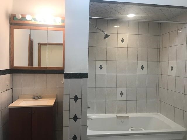 bathroom featuring tile walls, vanity, and tiled shower / bath