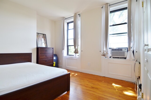 bedroom with multiple windows, cooling unit, and light wood-type flooring