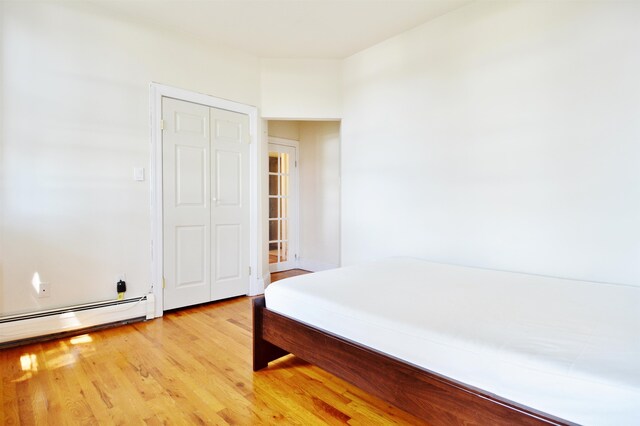 bedroom featuring light hardwood / wood-style floors, a closet, and a baseboard heating unit