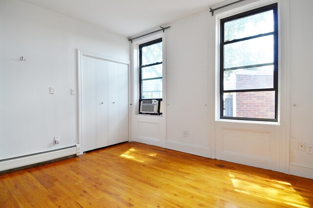 unfurnished room with light hardwood / wood-style floors, baseboard heating, and cooling unit