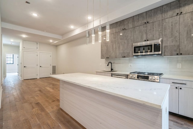 kitchen featuring appliances with stainless steel finishes, light hardwood / wood-style flooring, hanging light fixtures, sink, and a center island