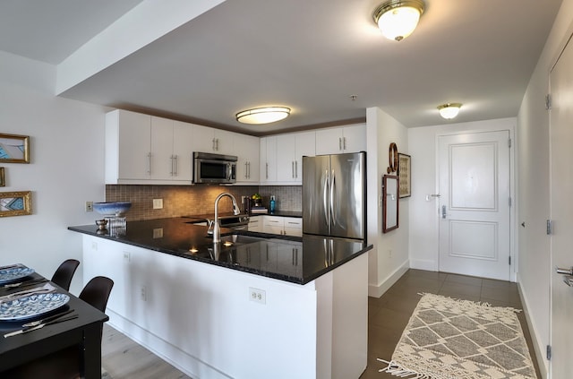 88 Morgan St Unit 2206, Jersey City, NJ 07302 - kitchen with stainless steel appliances, a peninsula, decorative backsplash, white cabinetry, and dark tile patterned flooring