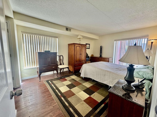 bedroom featuring baseboards, wood finished floors, visible vents, and a textured ceiling