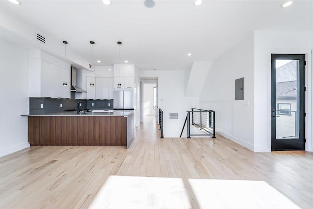 kitchen with hanging light fixtures, wall chimney range hood, light hardwood / wood-style floors, decorative backsplash, and white cabinetry