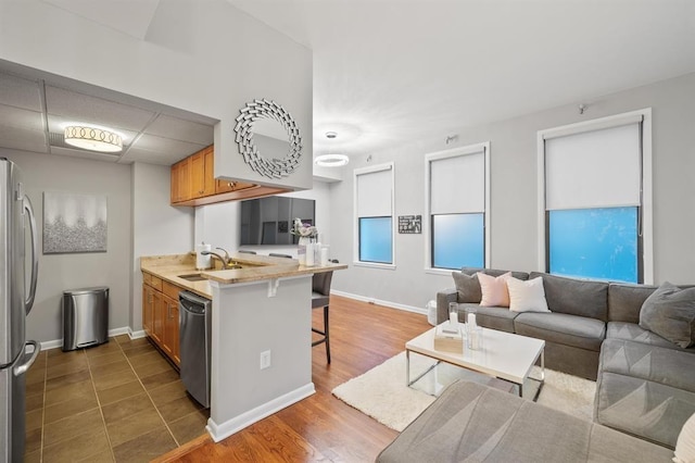 kitchen with appliances with stainless steel finishes, a peninsula, a breakfast bar area, a sink, and brown cabinetry