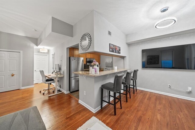 kitchen with stainless steel appliances, a breakfast bar area, brown cabinets, a peninsula, and wood finished floors