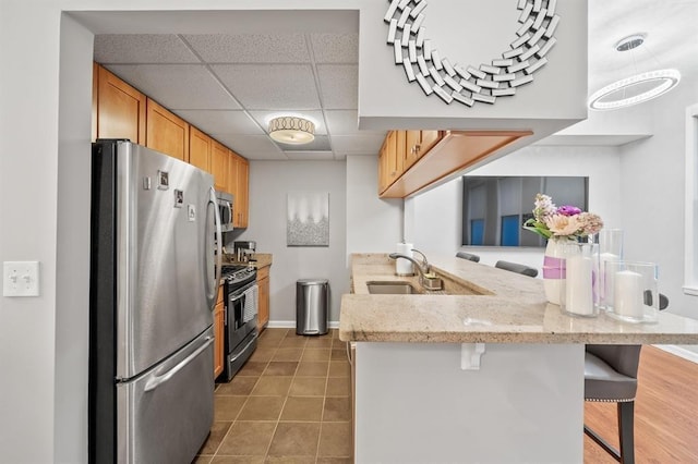 kitchen featuring appliances with stainless steel finishes, a drop ceiling, a peninsula, a sink, and a breakfast bar area