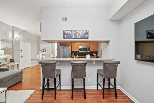 kitchen featuring stainless steel appliances, brown cabinetry, a breakfast bar, decorative backsplash, and wood finished floors
