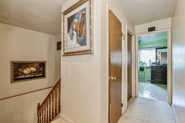 hall featuring a textured ceiling, baseboards, and carpet floors