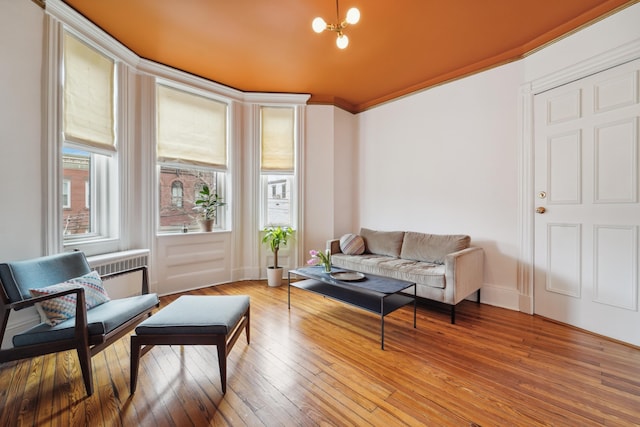 living area with light wood-style flooring, radiator, crown molding, baseboards, and a chandelier